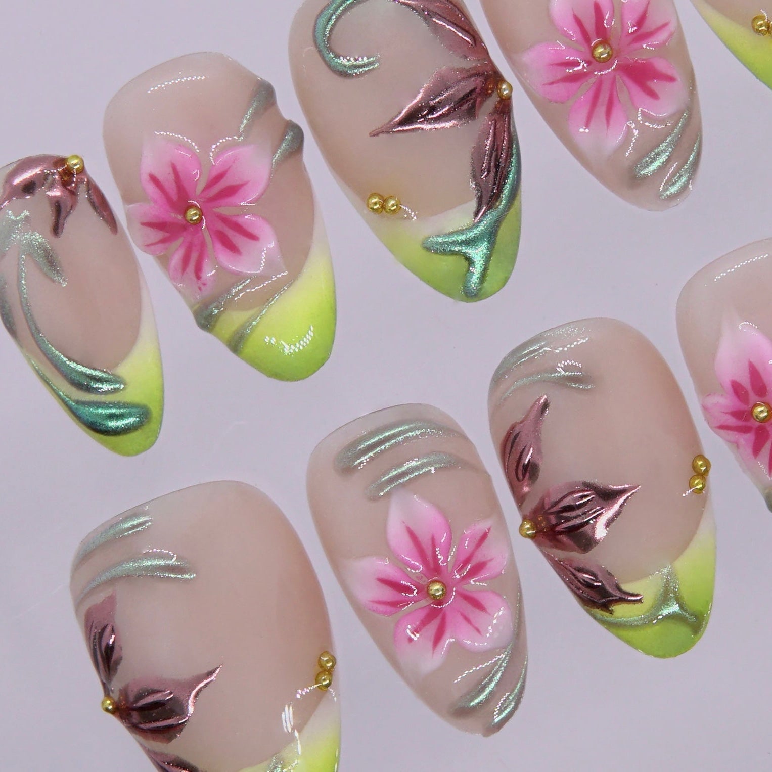 Detailed view of almond press on nails with nude base, soft pink blossom art, fresh green tips, and reflective metallic accents
，