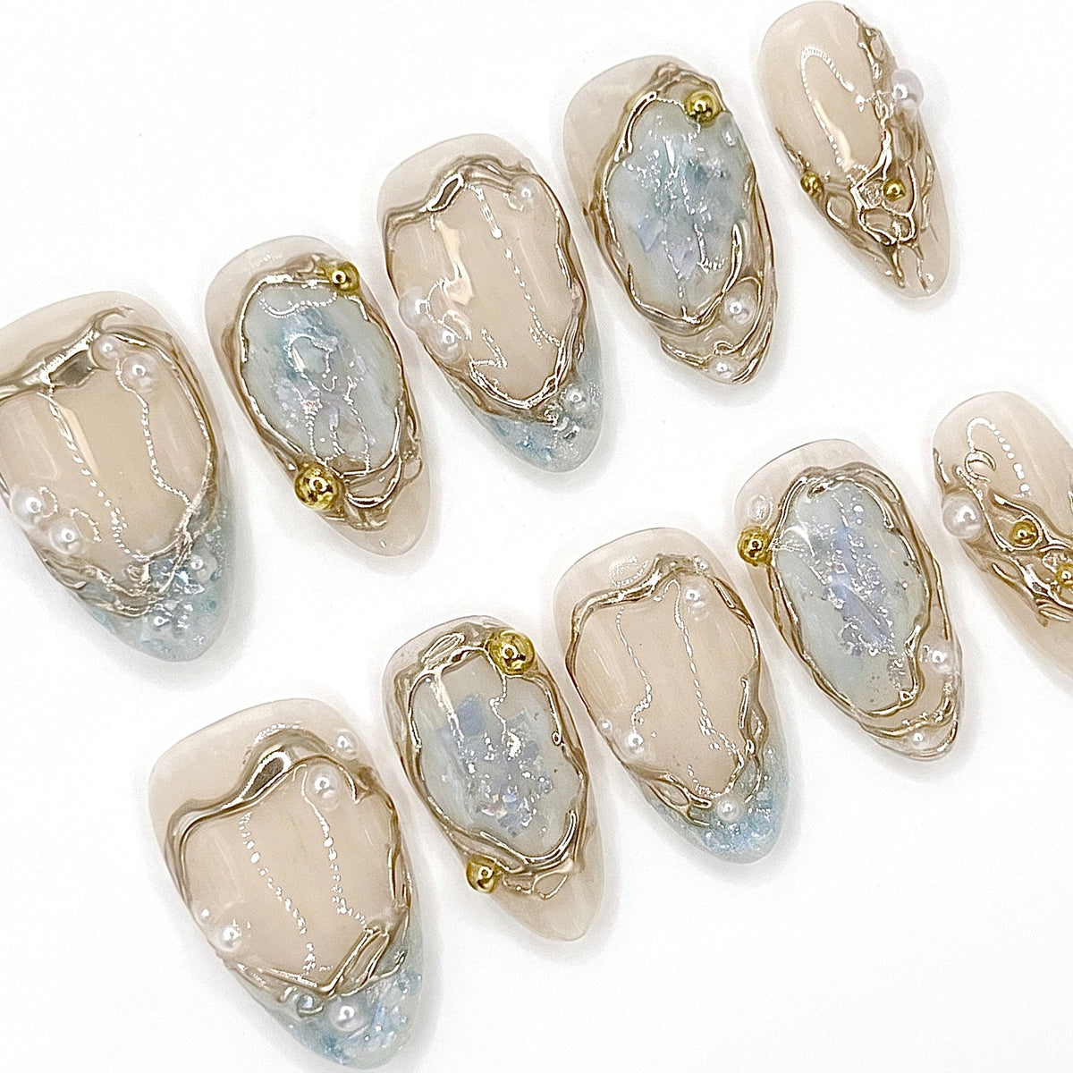 Close-up of Frosted Veil press-on nails featuring pale blue translucent details, irregular gold framing, pearl accents, and iridescent shimmer