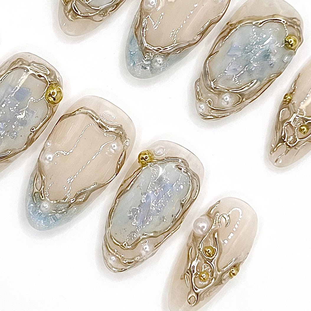 Detailed view of Frosted Veil nail art with glassi-like blue accents, dimensional gold frames, luminous pearls, and iridescent details