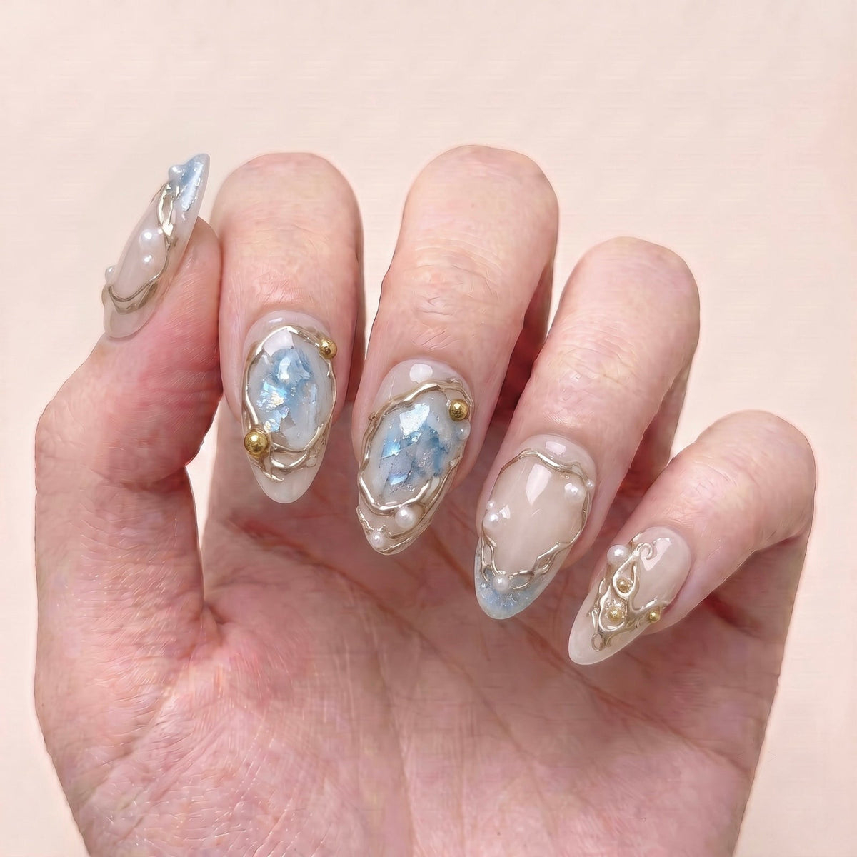 Frosted Veil handmade press-on nails worn on hand with sheer nude tones, soft blue accents, sculpted gold details, and pearls