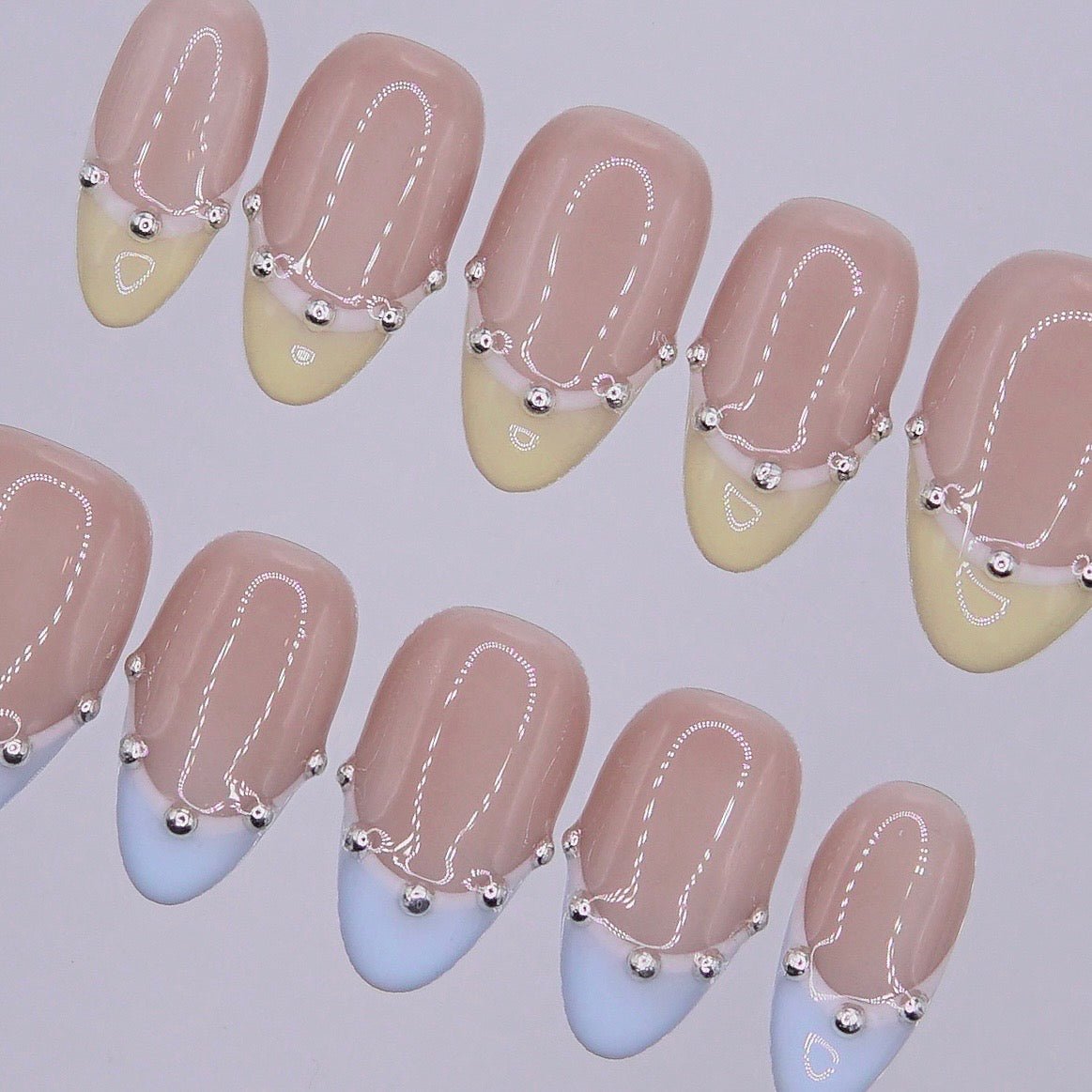 Close-up of handmade pastel French tip nails with glossy finish and elegant silver bead detailing.
