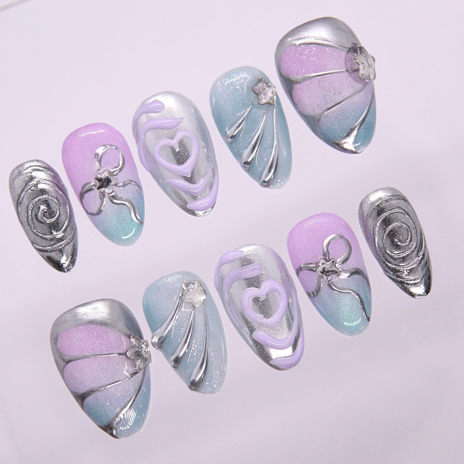 Flat lay of a pastel chrome nail set featuring sculptural silver lines and gradient tones.