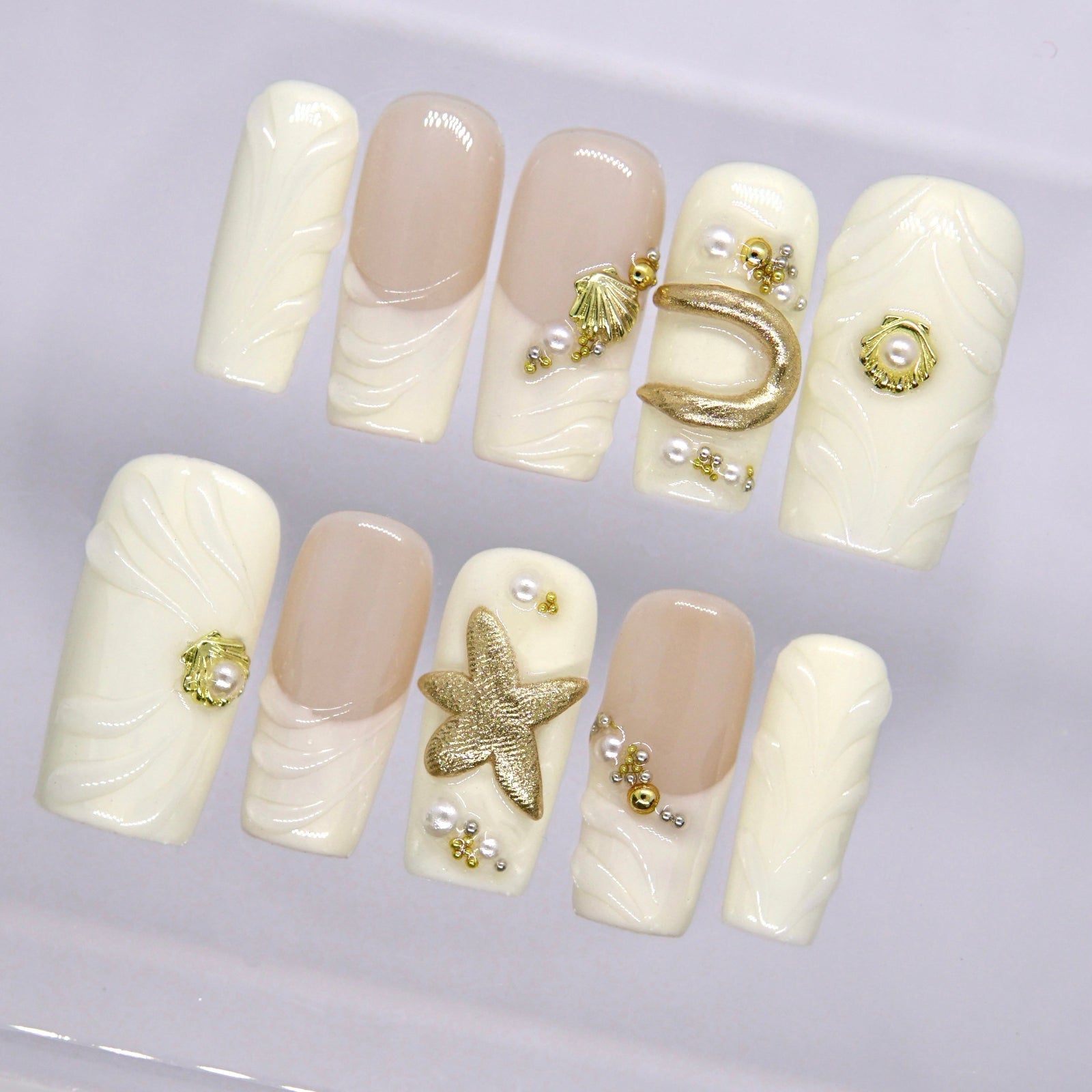 Detailed view of glossy long square nails with creamy white tones, nude accents, starfish detail, and elegant coastal embellishments