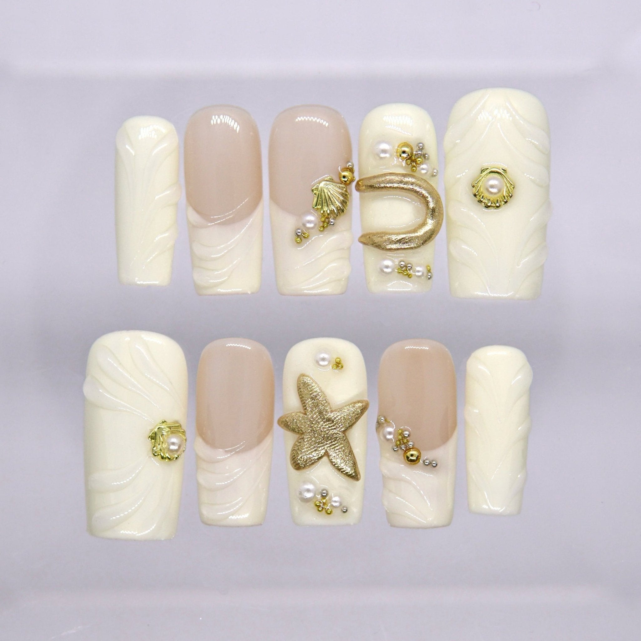 Long square press on nails in ivory and nude with gold shell, starfish, pearl details, and raised wave texture
