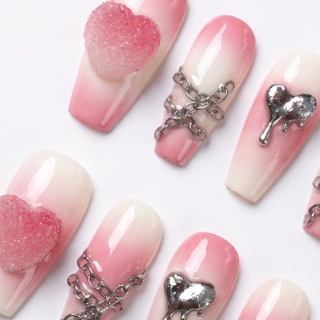 Close-up of silver chains and dripping heart charm on pink gradient press-on nails.