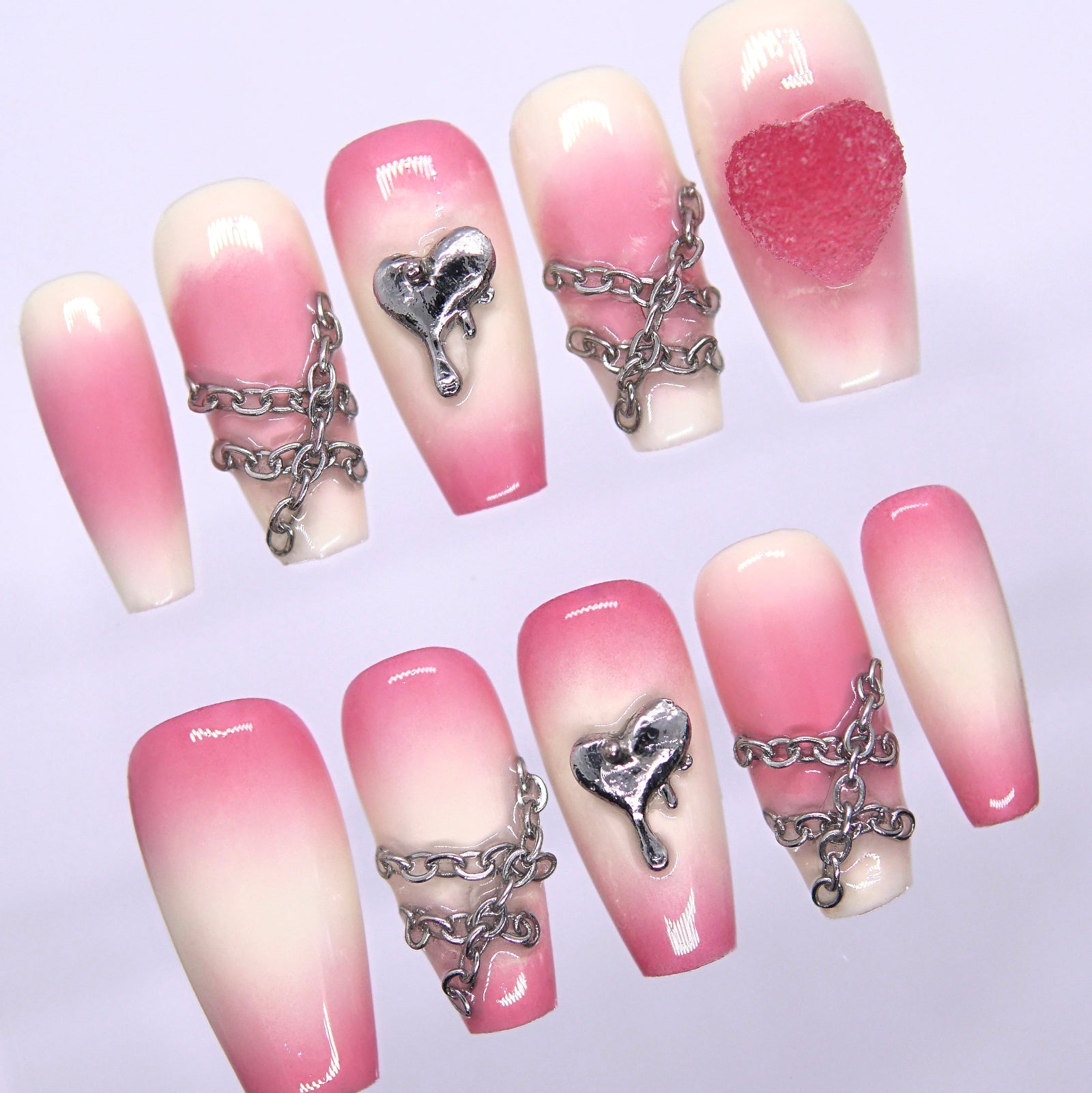 Close-up of silver chains and dripping heart charm on pink gradient press-on nails.
