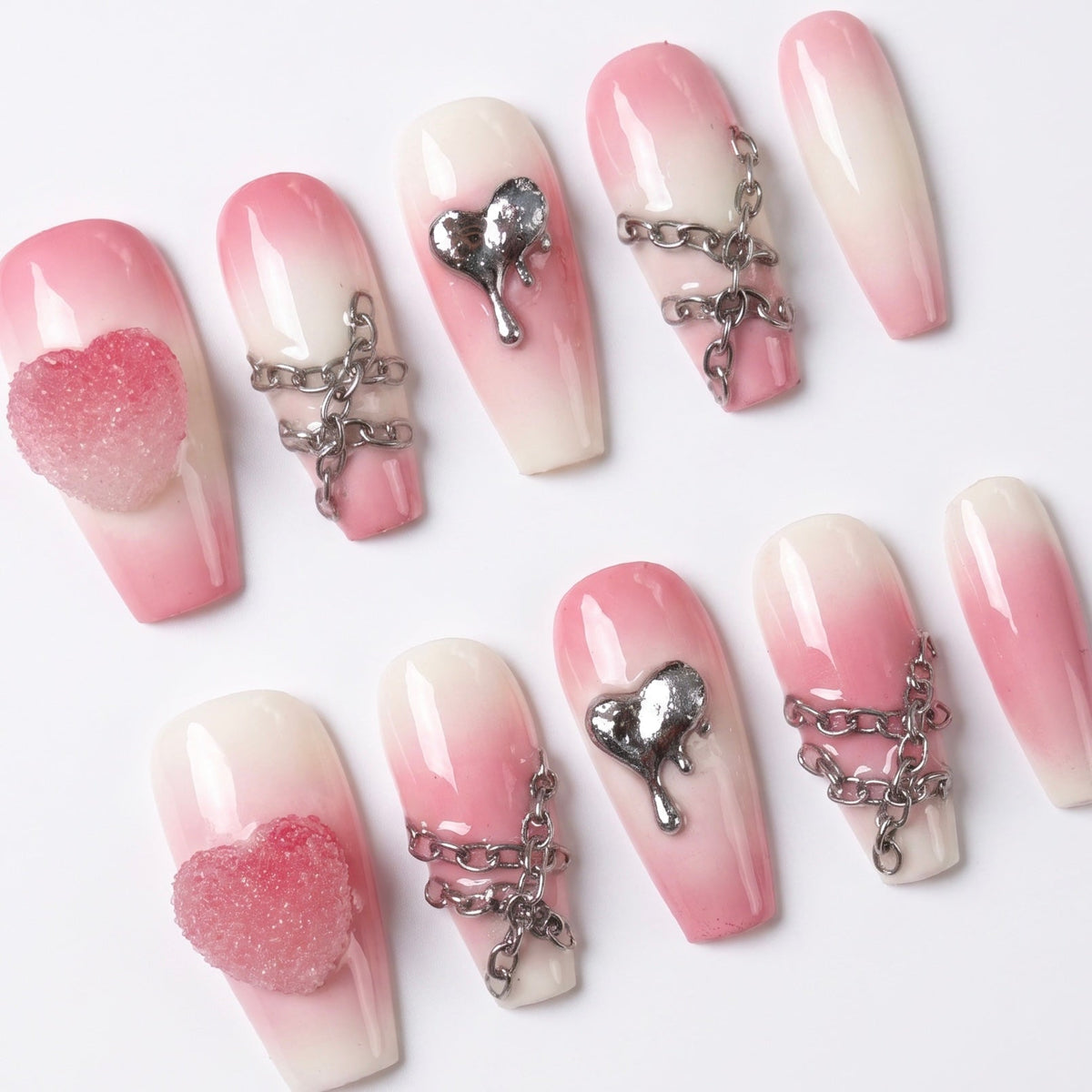 Close-up of silver chains and dripping heart charm on pink gradient press-on nails.