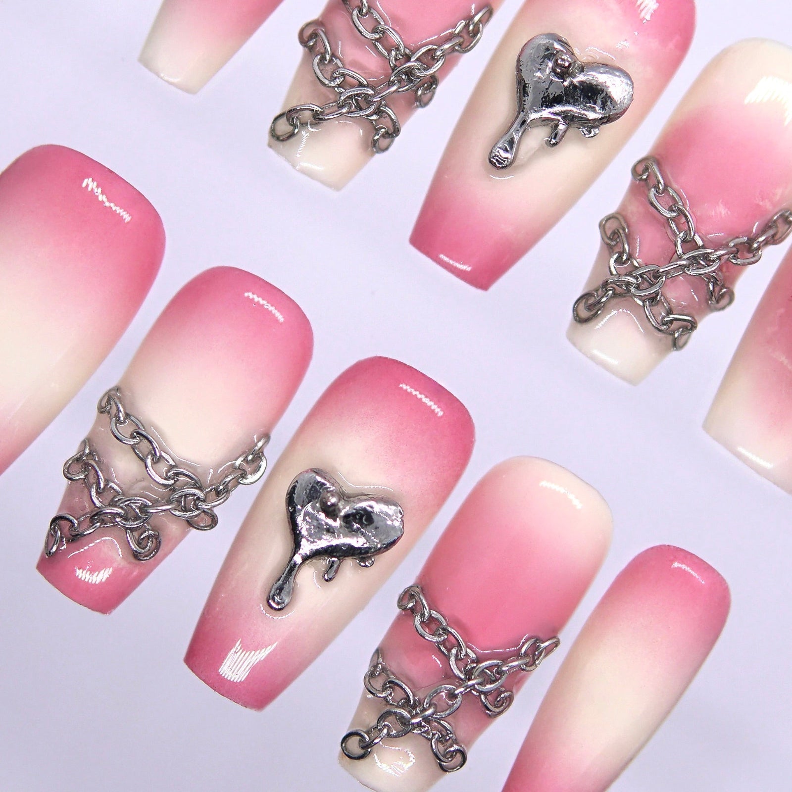 Close-up of silver chains and dripping heart charm on pink gradient press-on nails.