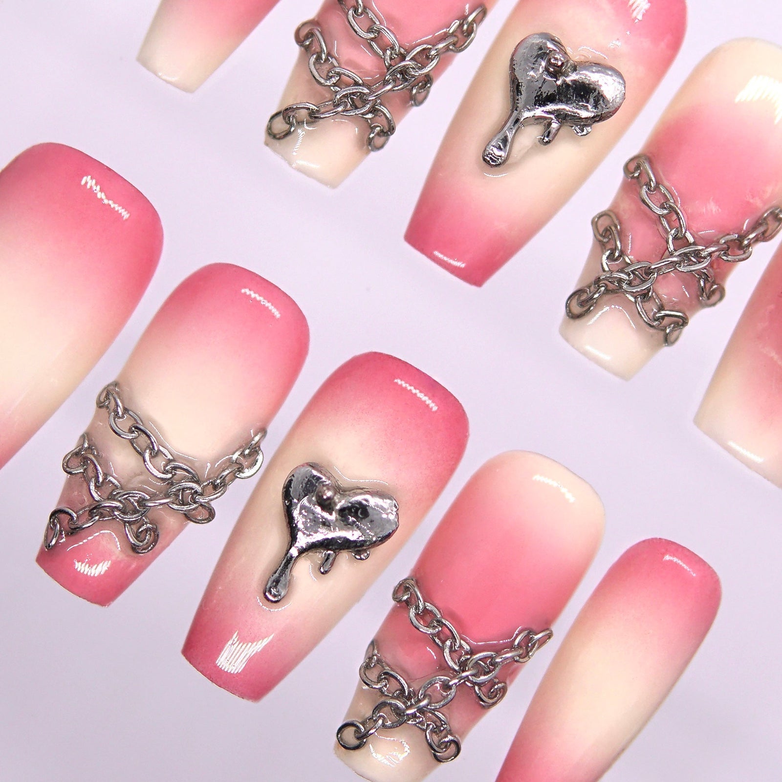 Close-up of silver chains and dripping heart charm on pink gradient press-on nails.
