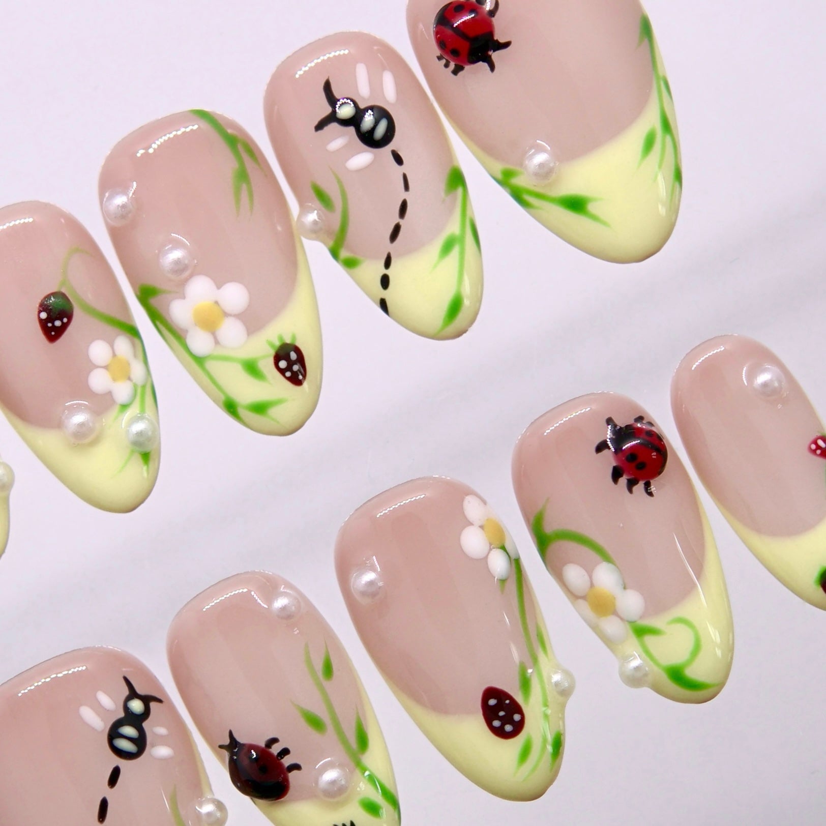 Cute spring press-on nails featuring ants, leaves, tiny fruit, and pearl accents