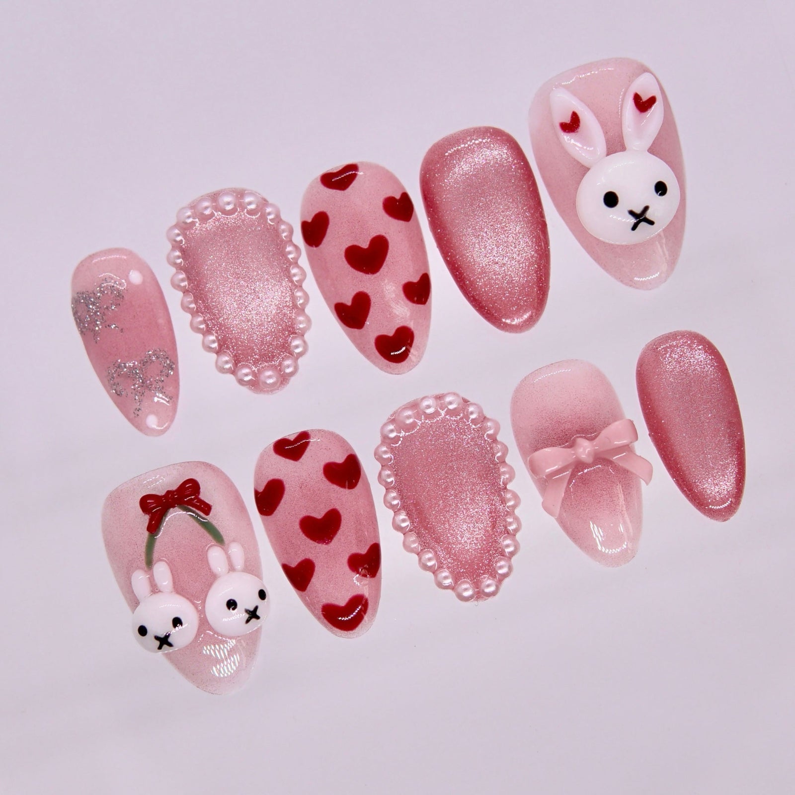 Close-up of Lullaby Rabbit press-on nails featuring blush pink shimmer base, heart designs, and pearl framed accent nails.