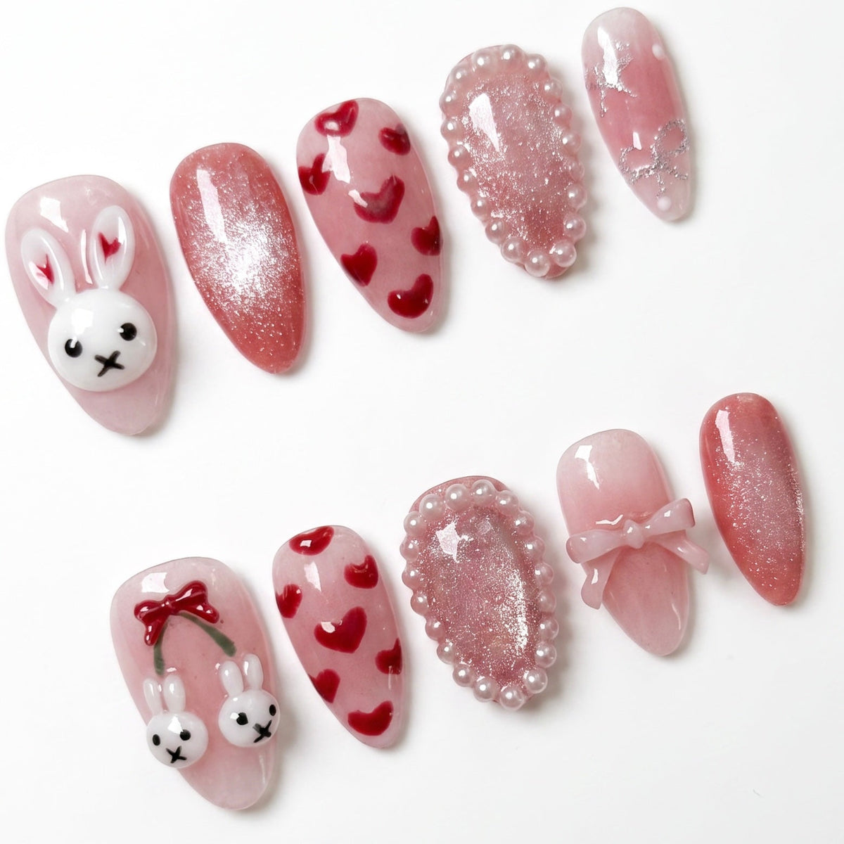 Close-up of Lullaby Rabbit press-on nails featuring blush pink shimmer base, heart designs, and pearl framed accent nails.