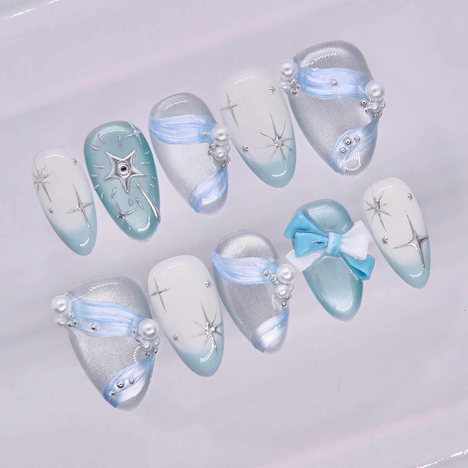 Close-up of blue nails with soft shimmer, pearl accents, and delicate bow charm