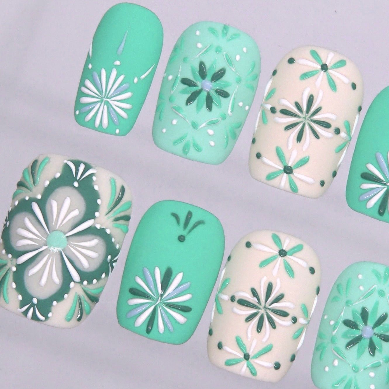 Detailed view of glossy short square nails with mint, cream, and green flower mosaic designs