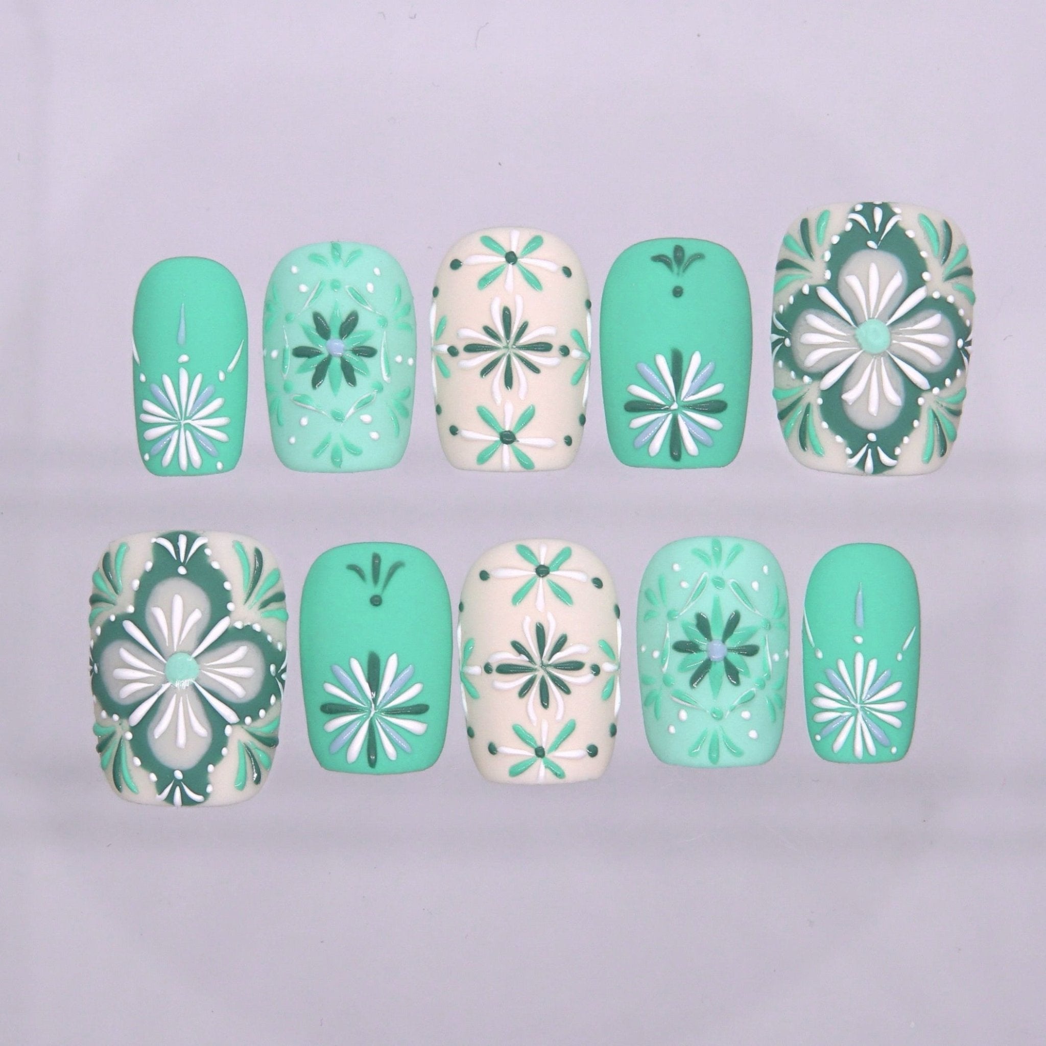 Short square press on nails in mint green and cream white with floral tile-inspired patterns and glossy finish
