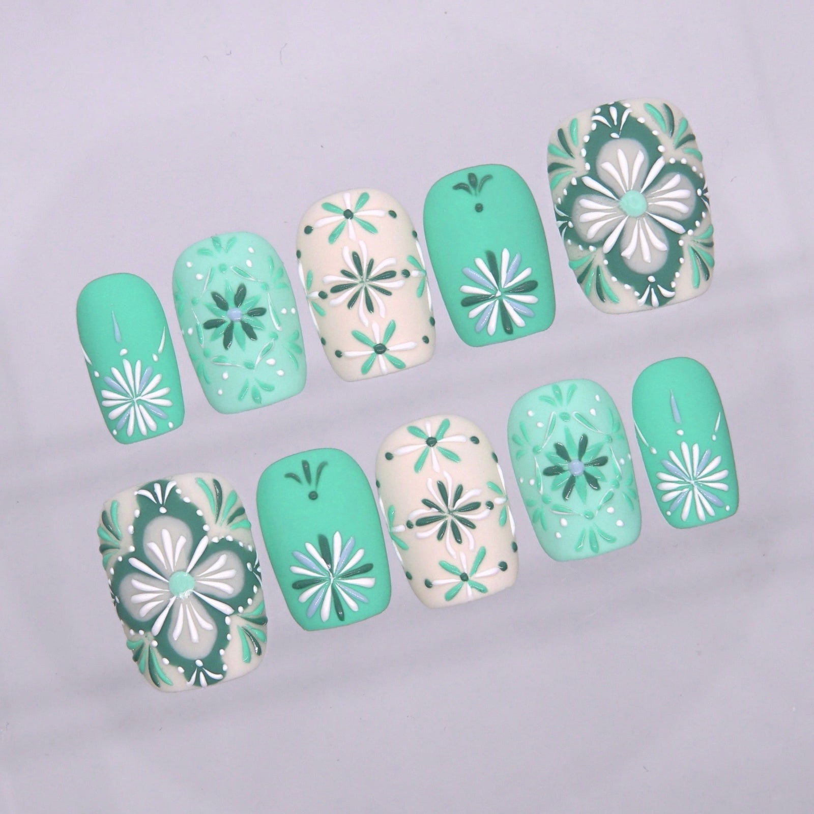 Close-up of mint green press on nails featuring white floral geometric details and vintage tile-inspired artwork