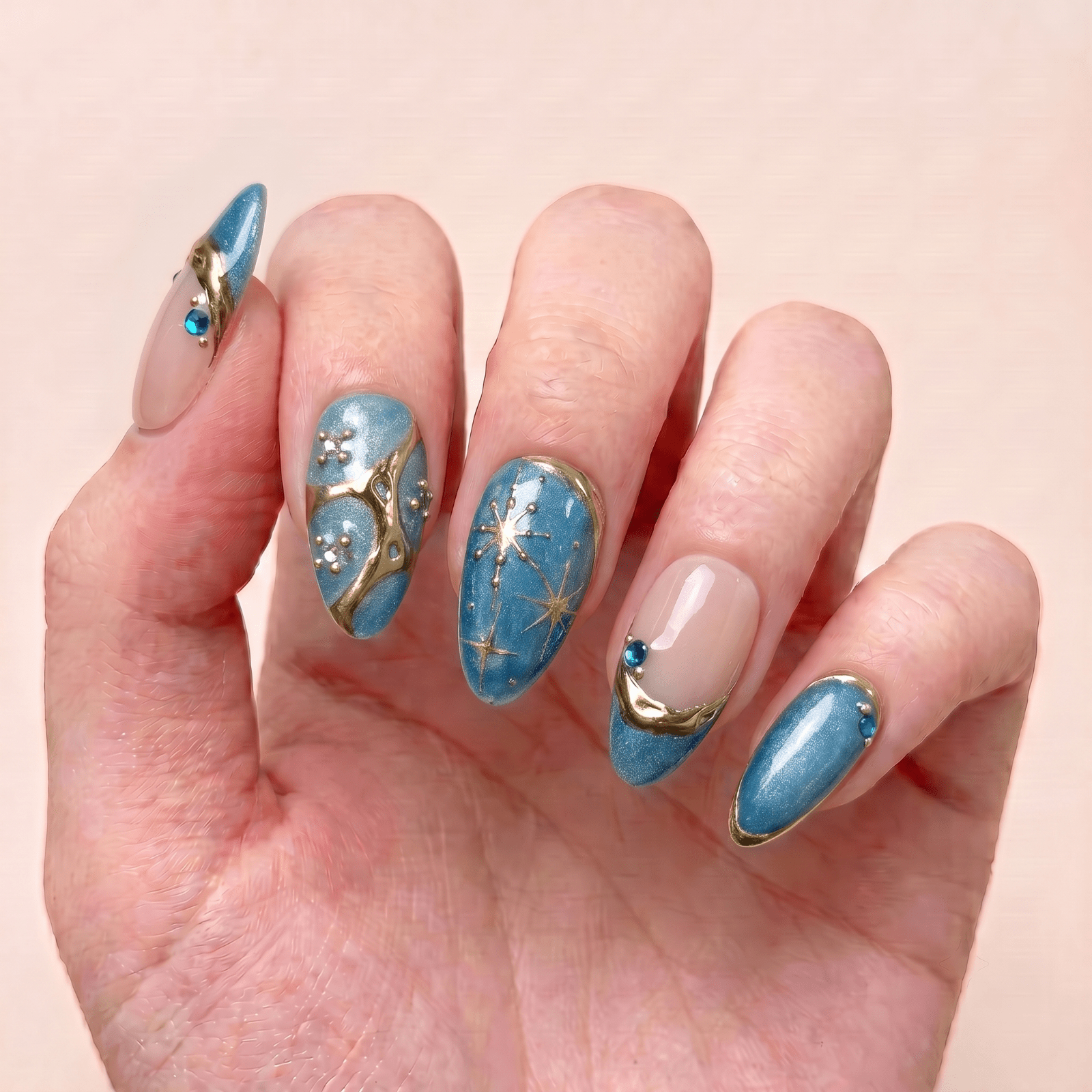 Moonlit Lagoon blue handmade press-on nails worn on hand with teal shimmer, gold details, pearl accents, and celestial designs