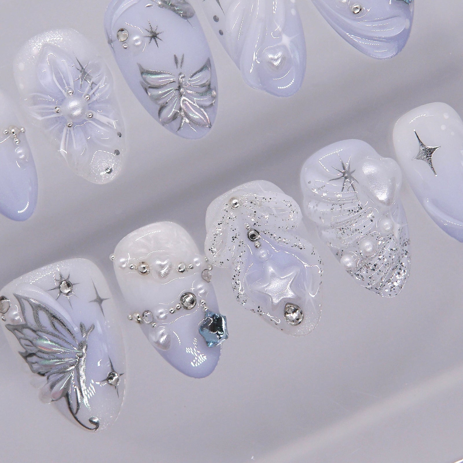 Soft pearly white and icy blue press-on nails with glowing pearls and glitter accents.
