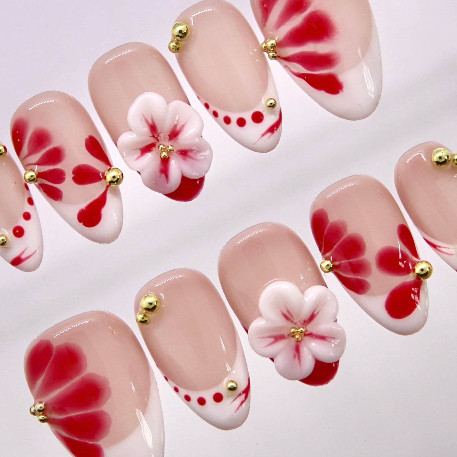 Close-up of red petal-inspired nail art with gold bead details