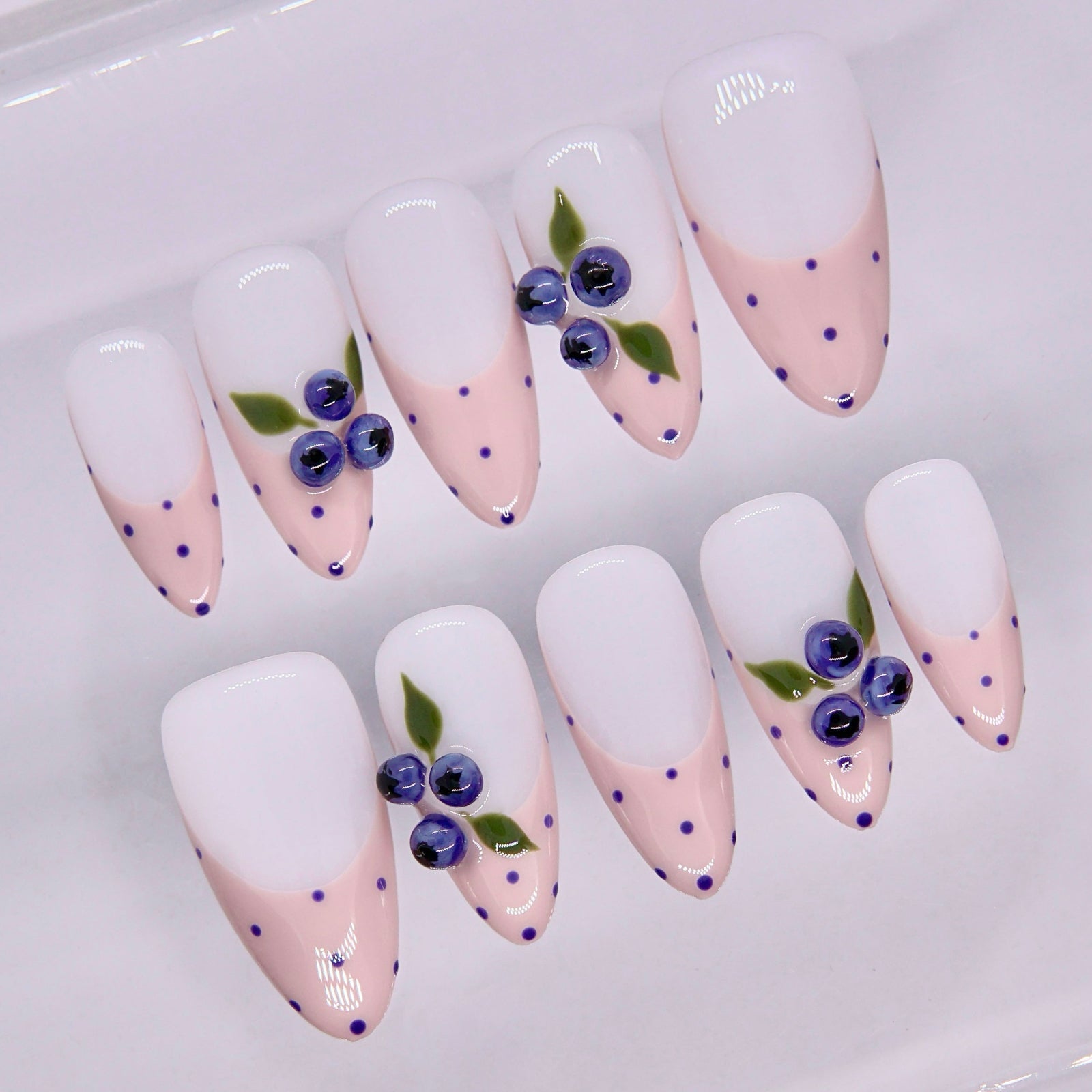 Close-up of pink nails with small blue dots and fruit detail accents