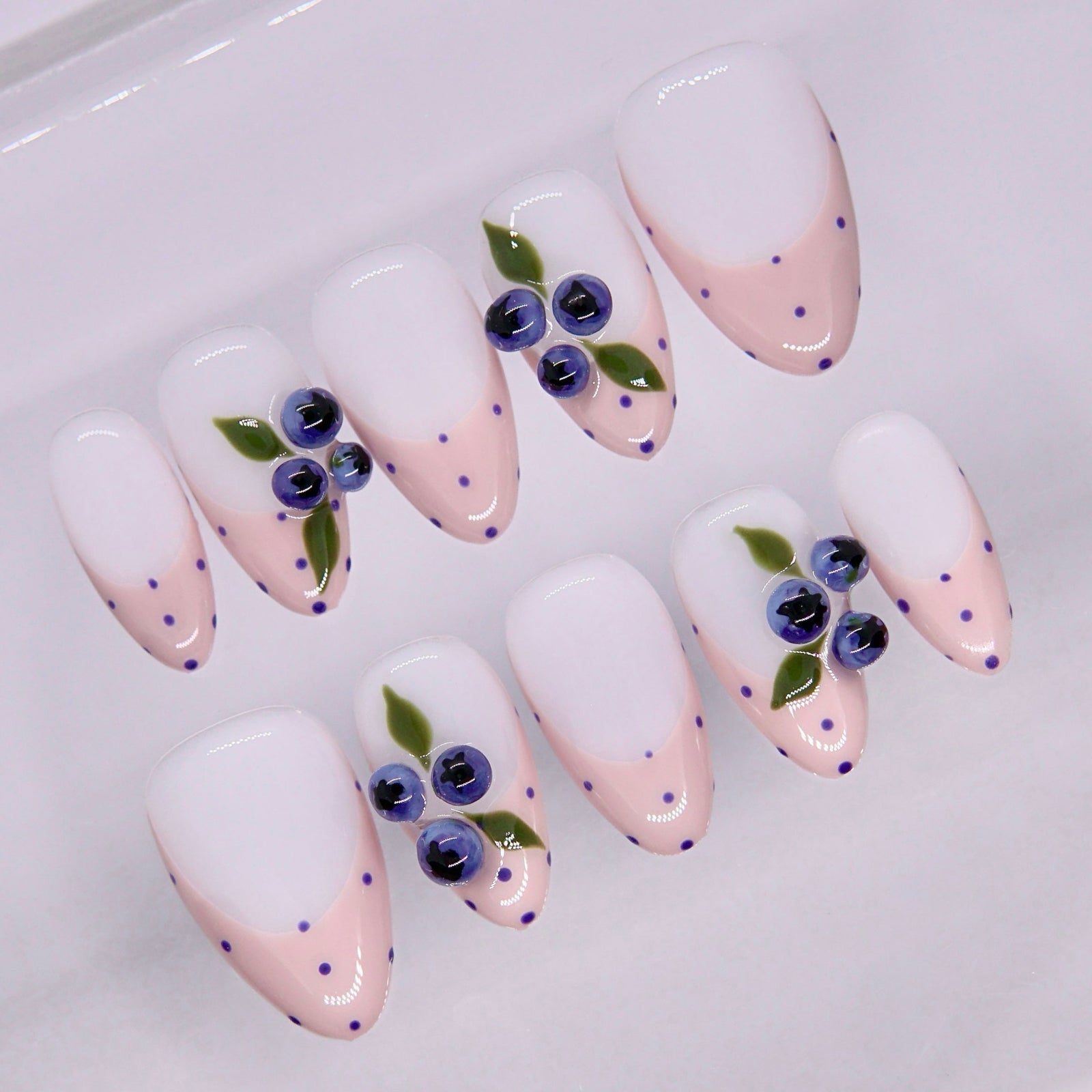 Close-up of pink nails with small blue dots and fruit detail accents