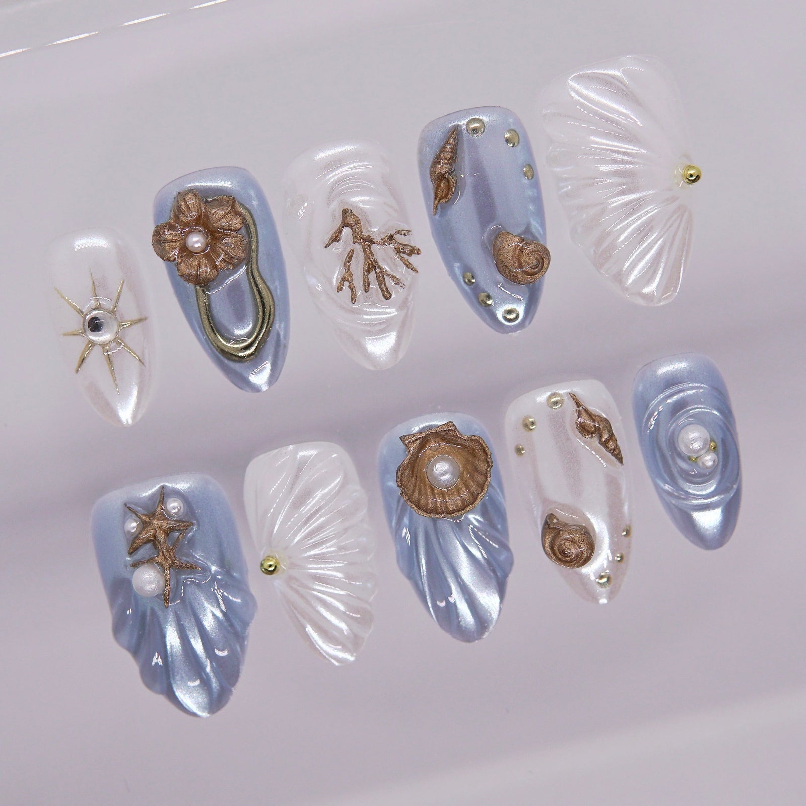 Close-up of 3D seashell press on nails featuring bronze ocean charms and pearl accents.