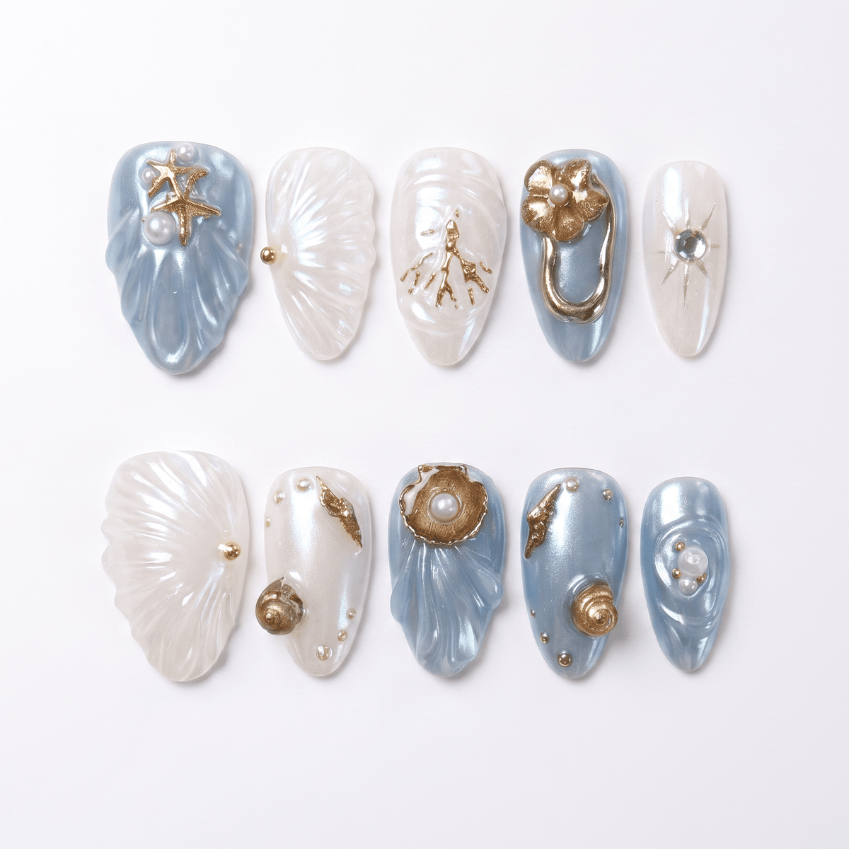 Press on nails with sculpted seashell design in pearl white and blue, decorated with bronze starfish, coral, and pearls. 