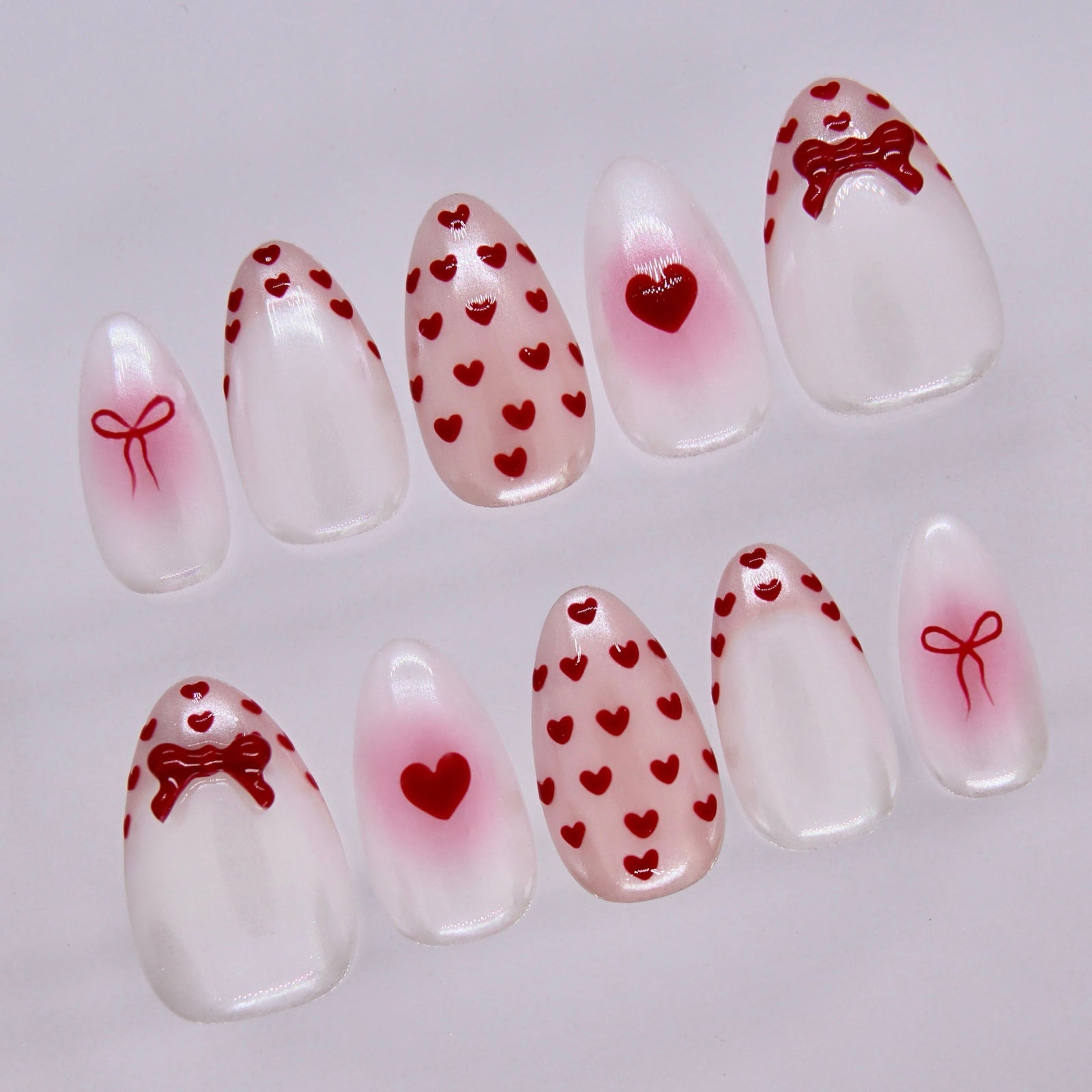 Close-up of Serene Goat press-on nails featuring glossy milky finish with red heart patterns and bow accents.