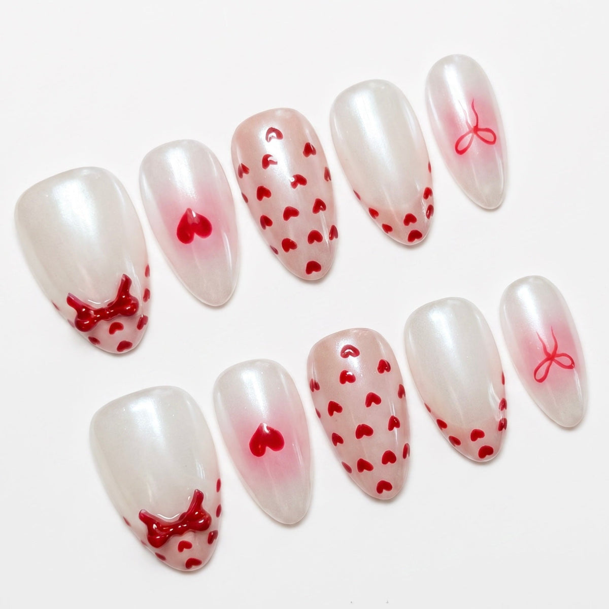Close-up of Serene Goat press-on nails featuring glossy milky finish with red heart patterns and bow accents.