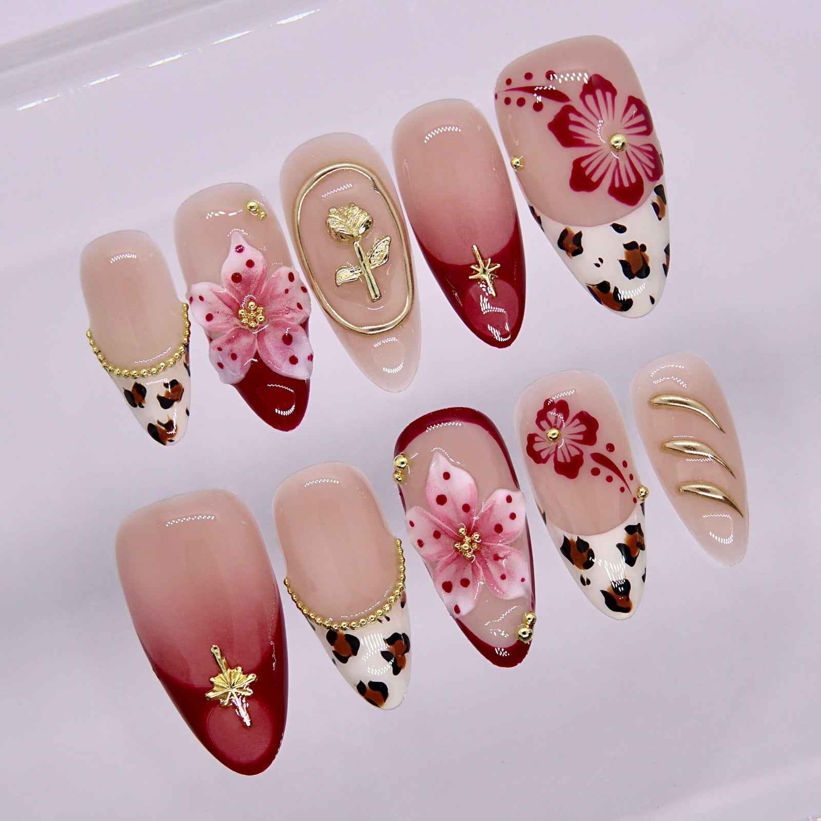 Close-up of red ombre nails with hand-painted flowers and gold embellishments