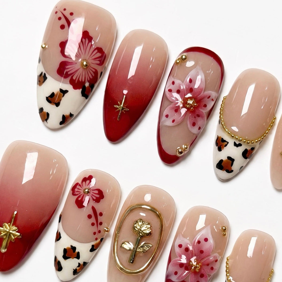 Close-up of red ombre nails with hand-painted flowers and gold embellishments