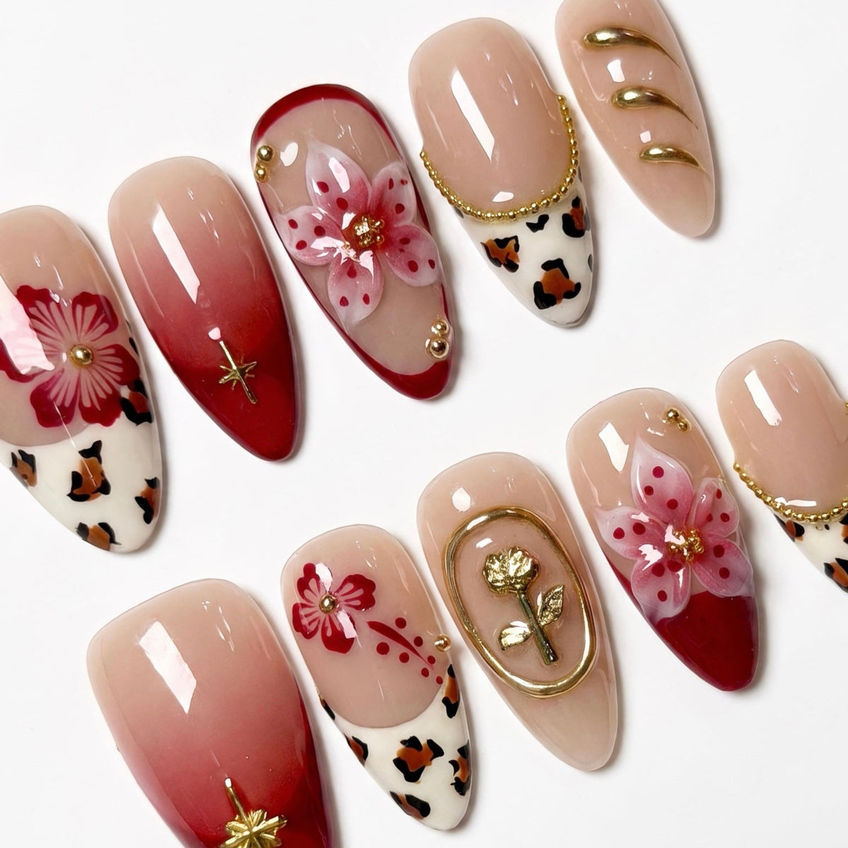 Close-up of red ombre nails with hand-painted flowers and gold embellishments