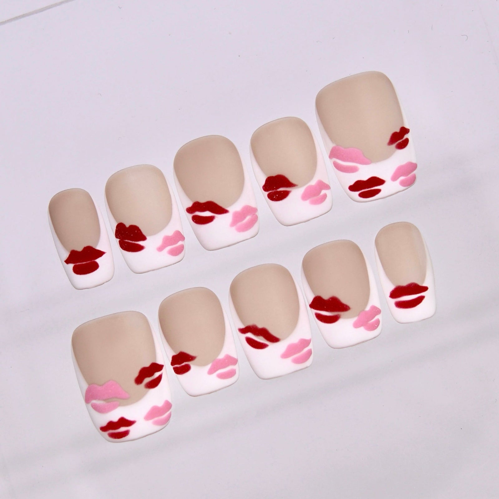 Close-up of Monkey Sparkle press-on nails featuring glossy red and pink lip accents on a soft nude matte base.
