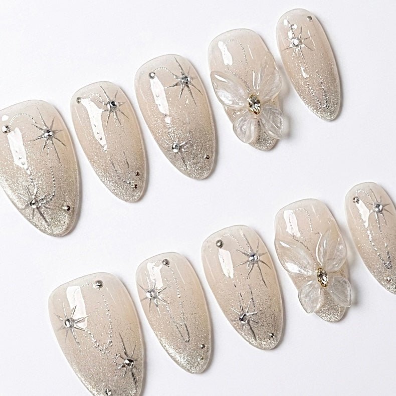 Close-up of Starlight Bloom press-on nails featuring champagne shimmer, delicate silver stars, crystal accents, and dimensional transparent flower details