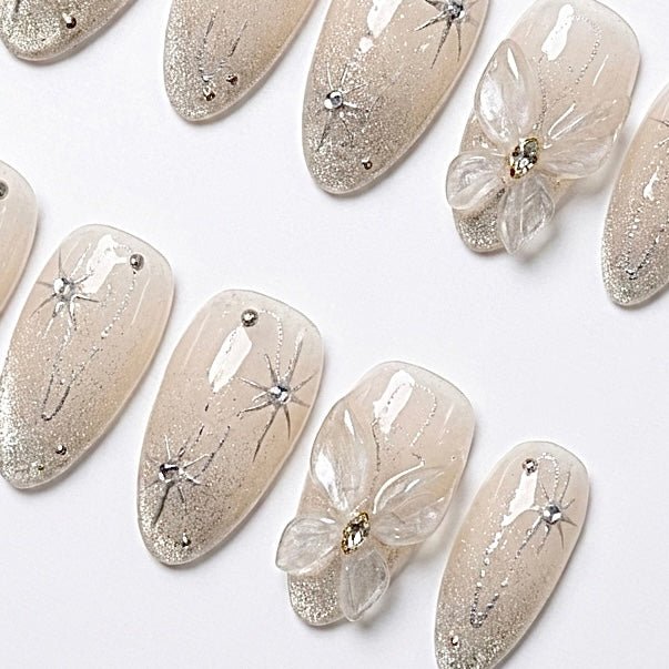 Detailed view of Starlight Bloom nail art with luminous champagne shimmer, silver star details, tiny crystals, and sculpted glass-like flowers
