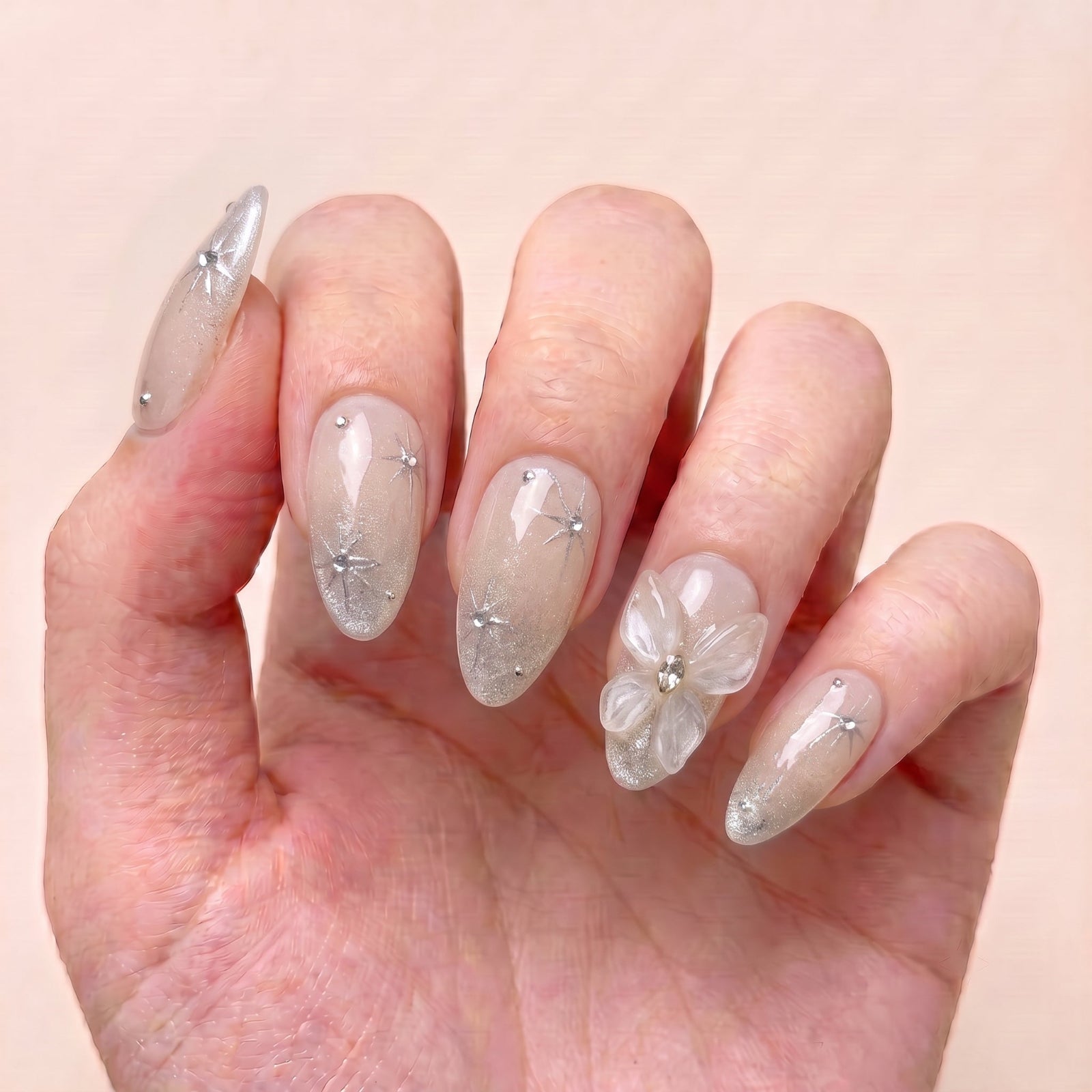 Starlight Bloom handmade press-on nails worn on hand with soft champagne shimmer, celestial starbursts, crystals, and translucent floral accents
