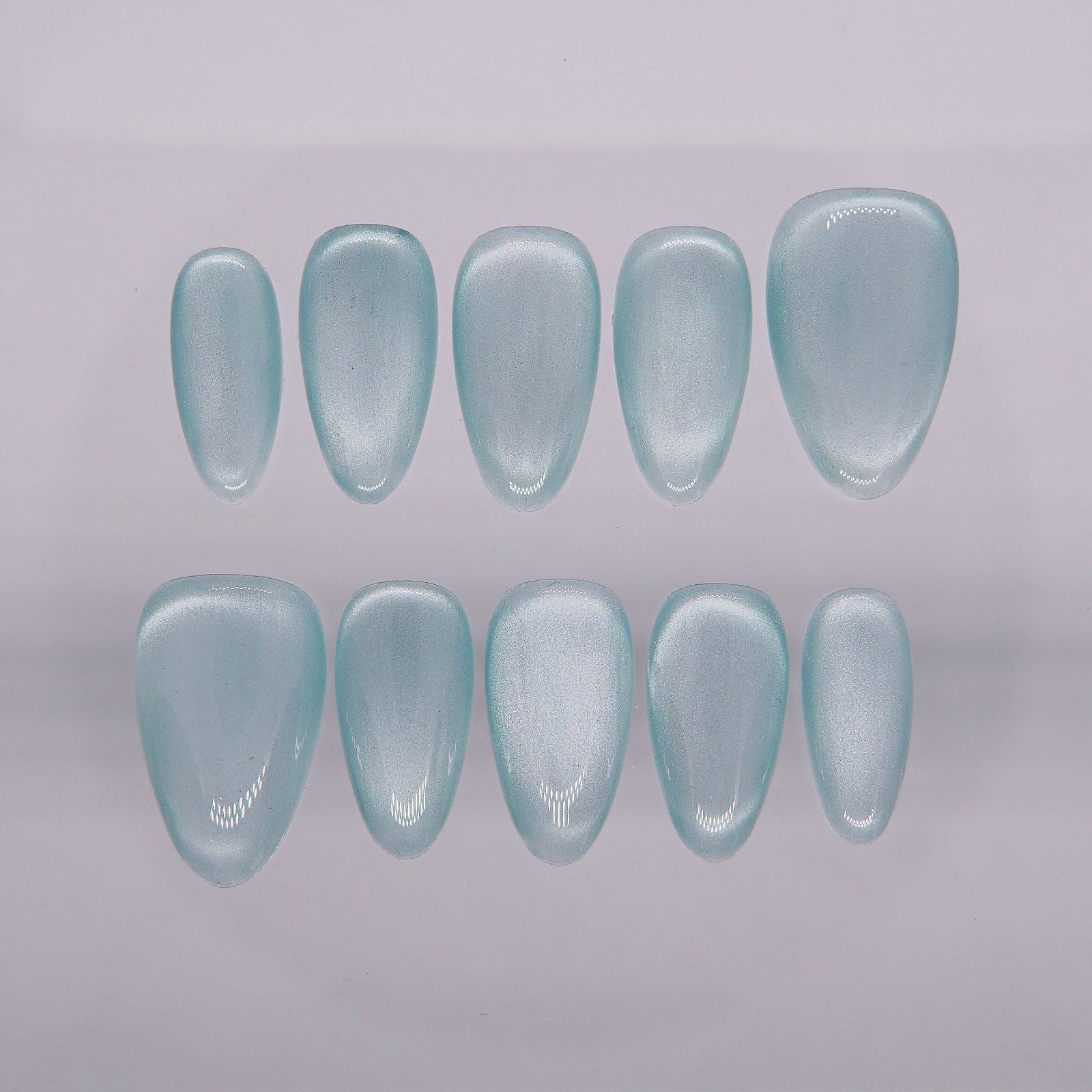 Dusty blue cat eye press on nails in almond shape, styled with ocean-inspired background.

