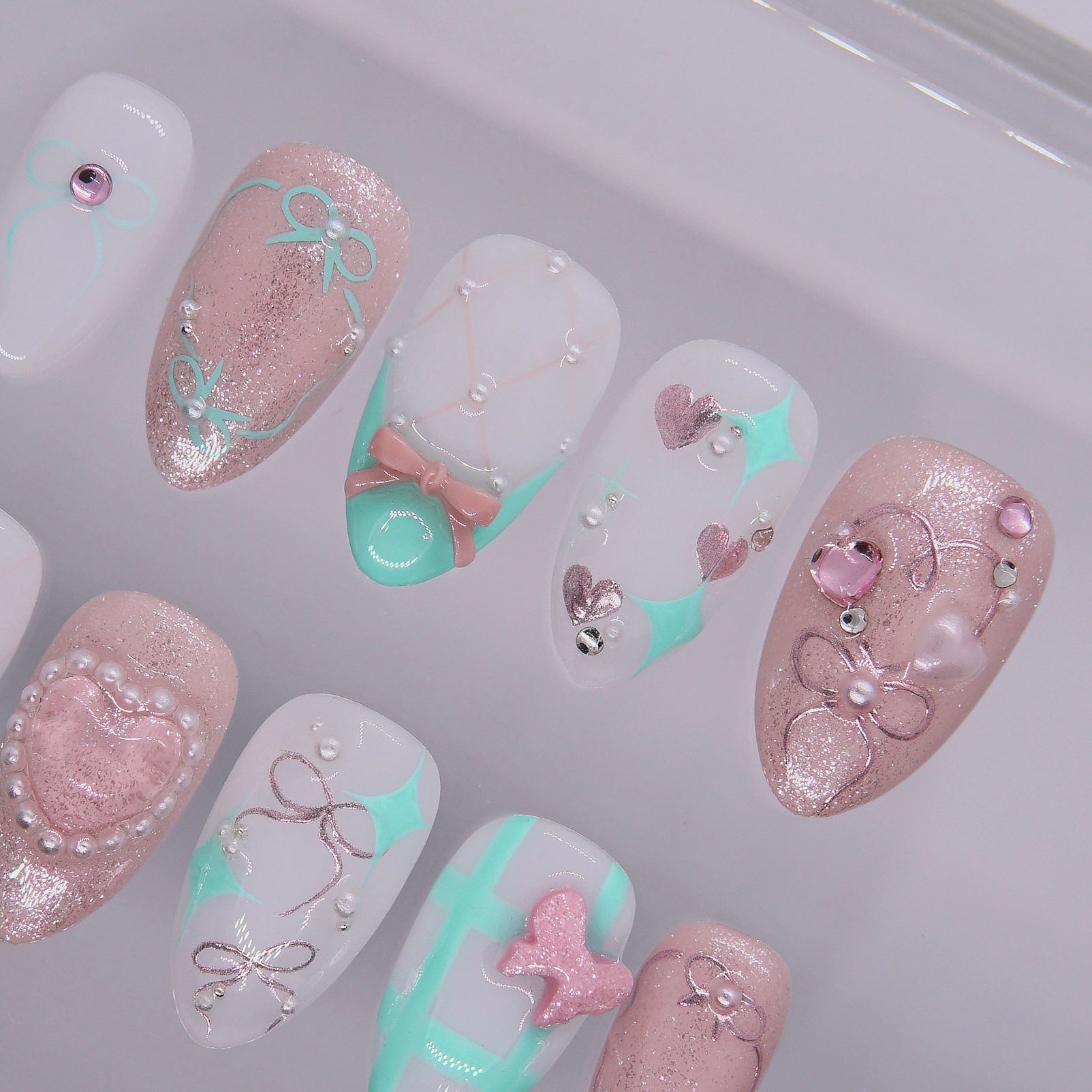 Close-up of pearl heart and pink glitter press-on nail with sculpted bow.