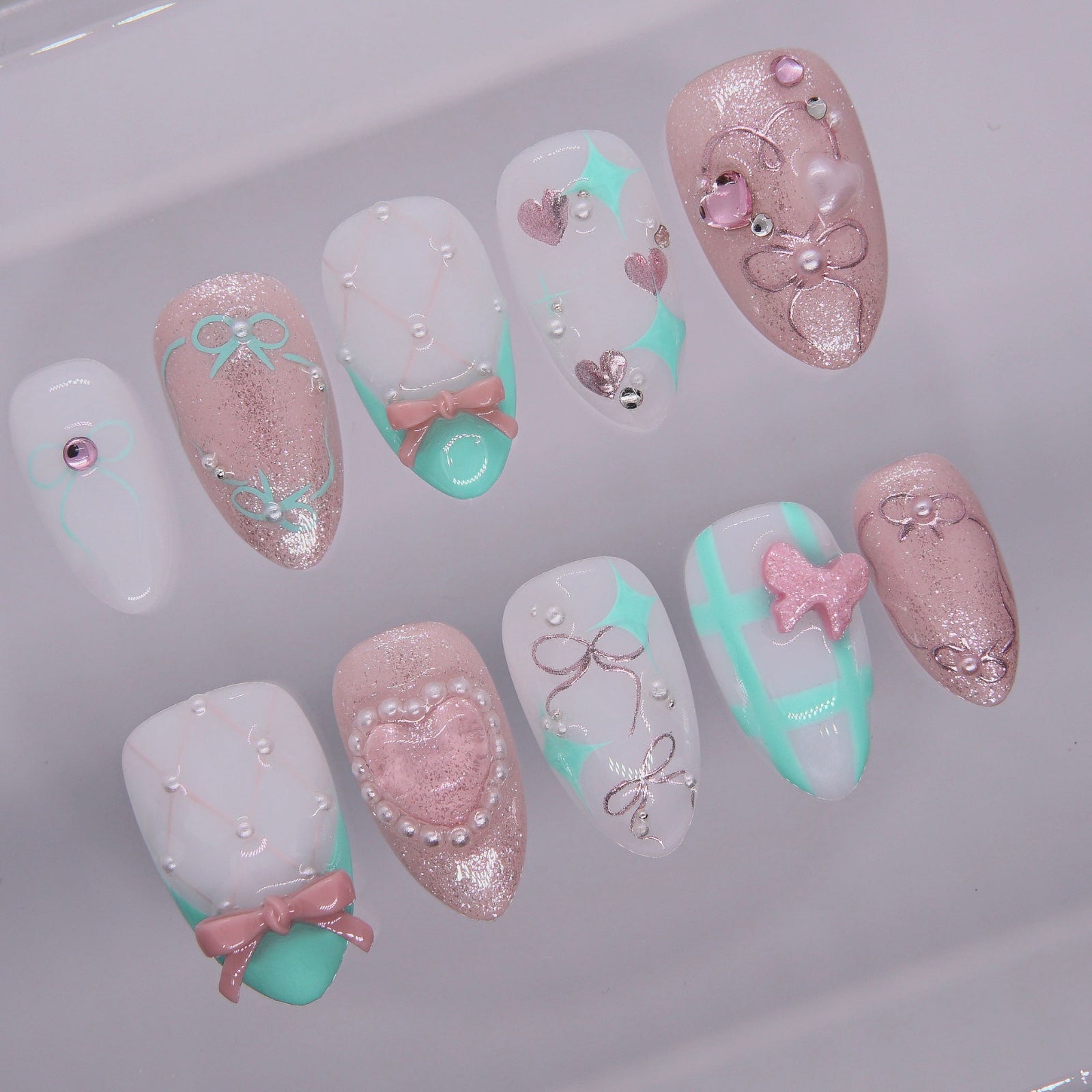Close-up of pearl heart and pink glitter press-on nail with sculpted bow.