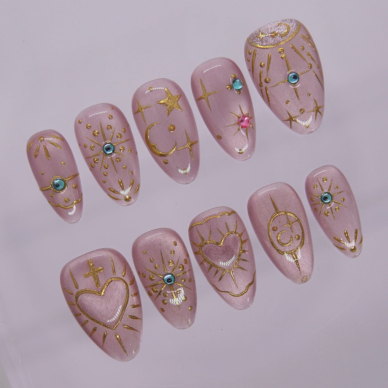 Close-up of hand-painted gold stars, hearts, and symbols on soft lilac press-on nails.